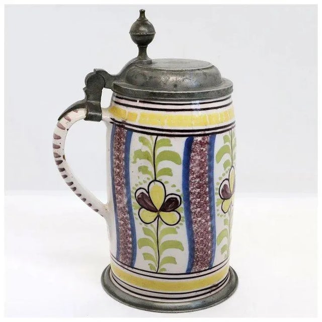 DETAILS An antique German in-glazed earthenware stein with vertical bands of polychrome floral decoration in yellow, blue,...