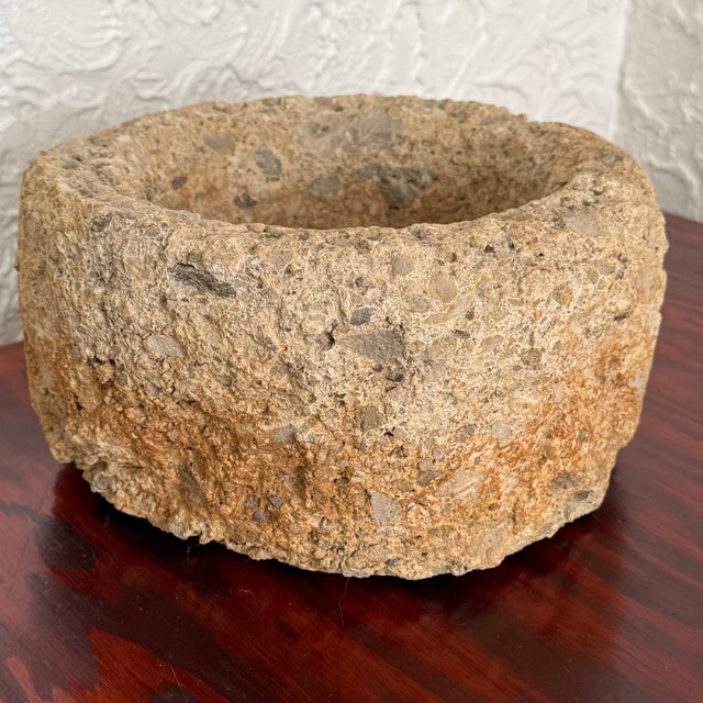 Round stone bowl with a thick rolled rim and a rough, pitted surface. The sand and cream tones look naturally weathered....