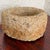 Round stone bowl with a thick rolled rim and a rough, pitted surface. The sand and cream tones look naturally weathered....