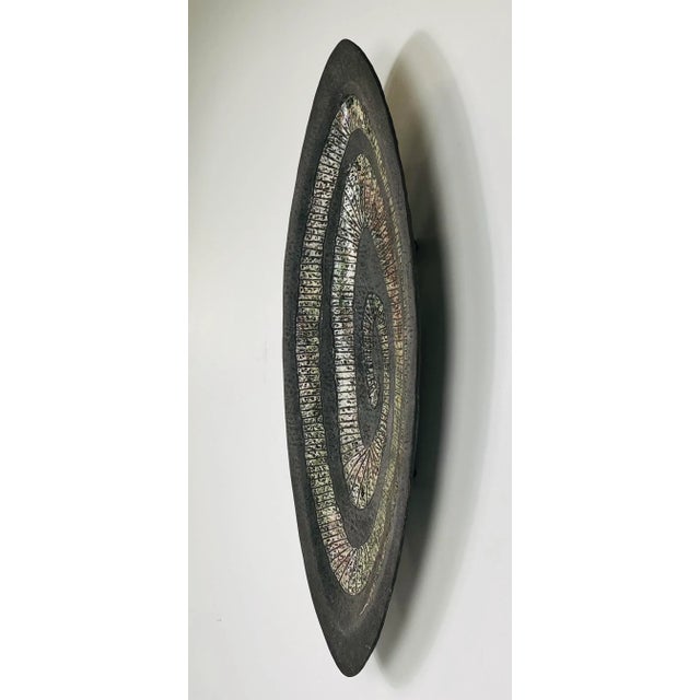 A unique metallic sculpture platter with an earth tone palette is footed with an elongated bowl designed by American...
