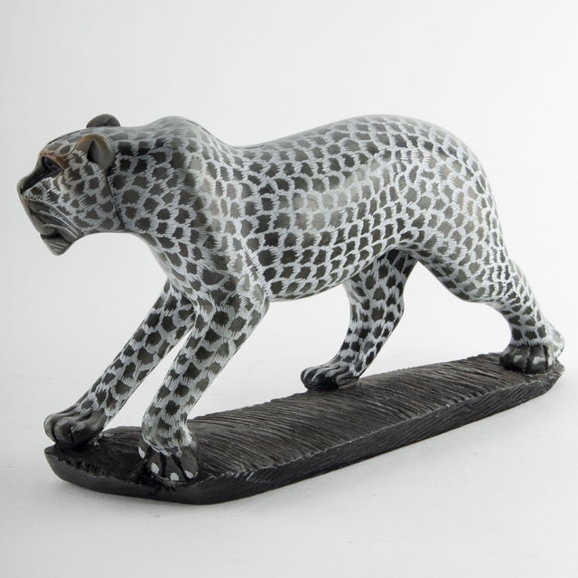 A finely carved soapstone figure of a leopard depicted in a prowling stance, the elongated body striding across a textured...
