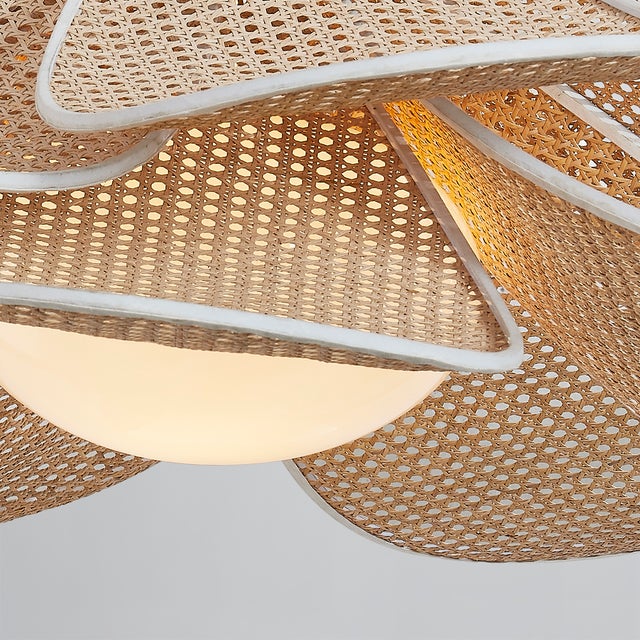 Petals of natural rattan caning are trimmed in white cotton and layered around an opal glossy glass globe to give Florina...
