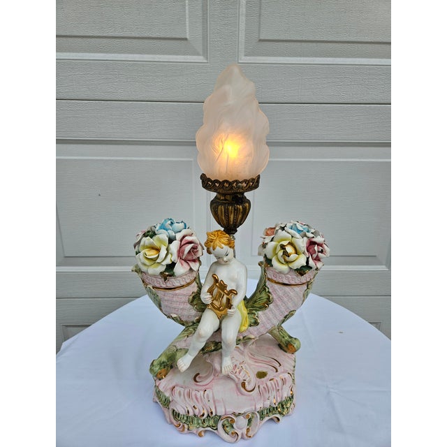 This fanciful cherub with lyre, set against a double cornucopia of flowers, is truly beautiful to behold. The lamp...