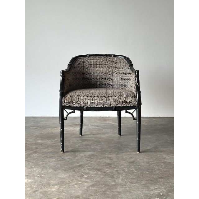 A black lacquered faux bamboo armchair with a barrel-shaped back, turned bamboo-style frame, and fretwork brackets at the...