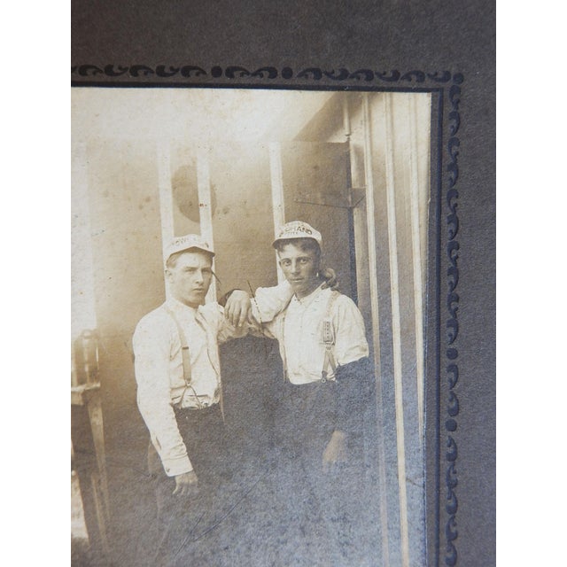 Antique late 19th century silver gelatin photograph mounted on gray cardboard backing. Two young men in suspenders and...