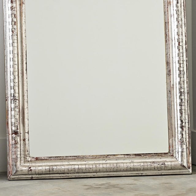 A French 19th century Louis Philippe mirror in a tall, silver gilt frame enhanced by dark oxidation and craquelure...