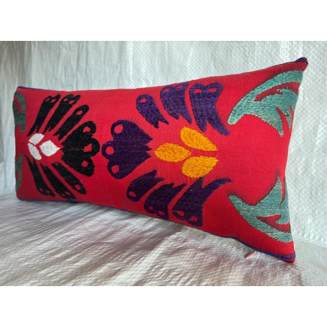 A striking early 1900s Suzani pillow featuring vivid hand embroidery in bold black, purple, and saffron tones over a deep...