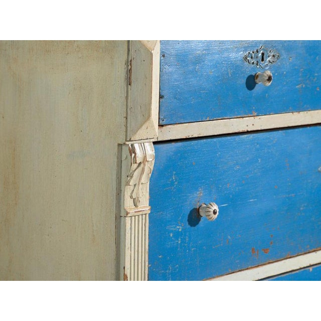 This antique painted chest of drawers in pine is a drawer cabinet with painted fronts and ceramic knobs, on bun feet. It...