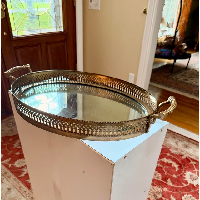 Glamorous mid-century oval vanity and barware tray featuring a reflective glass mirror base enclosed by an intricate,...