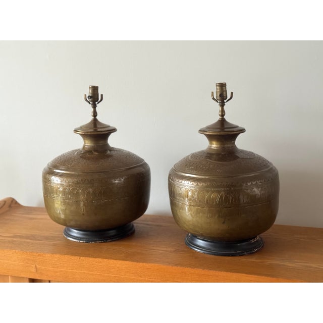 Pair of large brass urn-form table lamps. Rounded bodies with engraved foliate and geometric banding. Domed shoulders with...