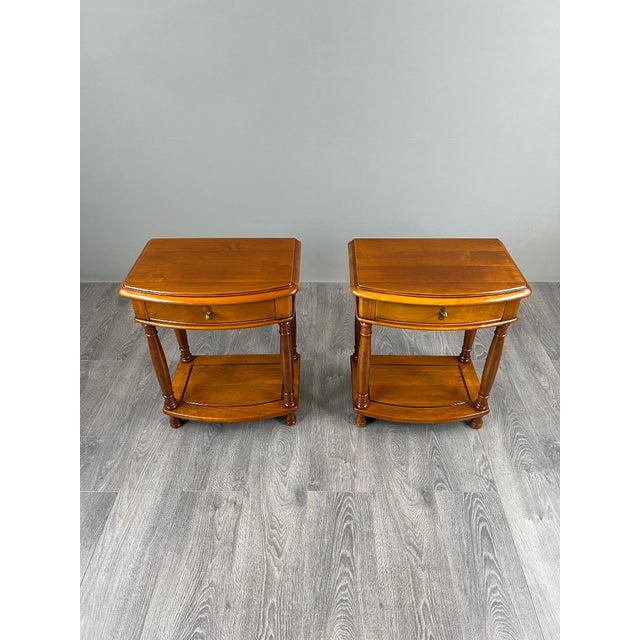 Pair of wooden bedside tables, resting on four turned legs. Each table features a drawer on the front, adorned with a...