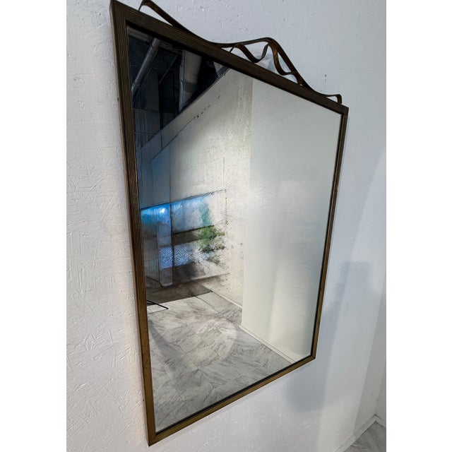 Rectangular vintage wall mirror featuring a finely ribbed brass-toned frame and a decorative wavy metal ribbon detail...
