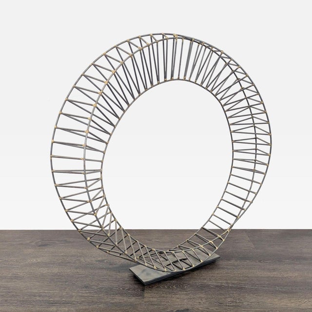 This modern metal sculpture features a circular wire design with an open center. The structure is made from sturdy metal...