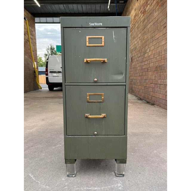 Rare industrial military green two drawer file cabinet from Shaw Walker, having brass hardware, and lucite cube feet,...