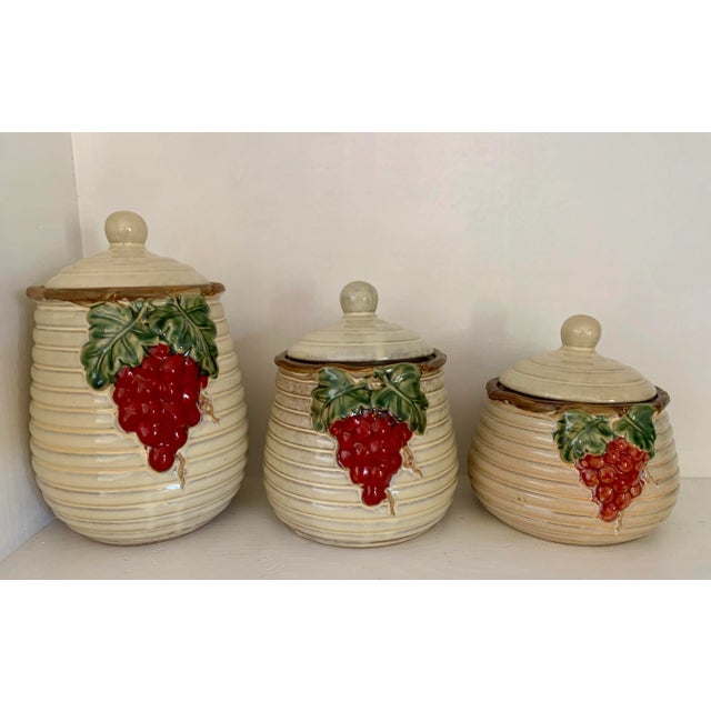 A light colored beehive shaped set of kitchen canisters with lids. The containers have 3 different sizes and are decorated...