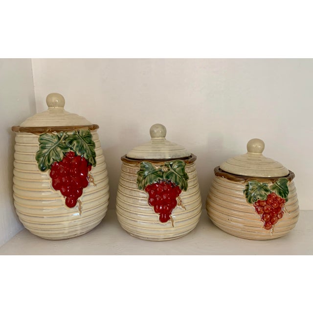 A light colored beehive shaped set of kitchen canisters with lids. The containers have 3 different sizes and are decorated...