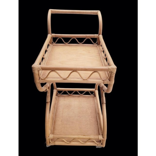A wonderful vintage 2 tier hand-woven rattan bar cart on wheels. It features an organic design with a natural light blond...