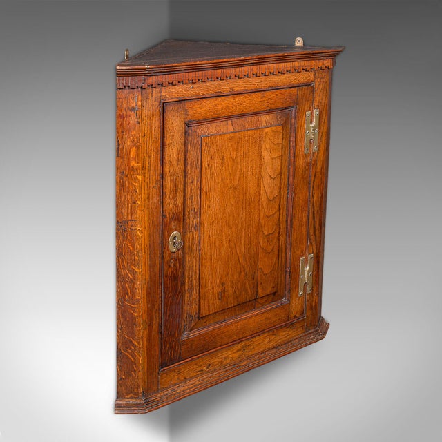 This is a small antique corner cabinet. An English, golden oak hanging cupboard, dating to the Mid Georgian period, circa...