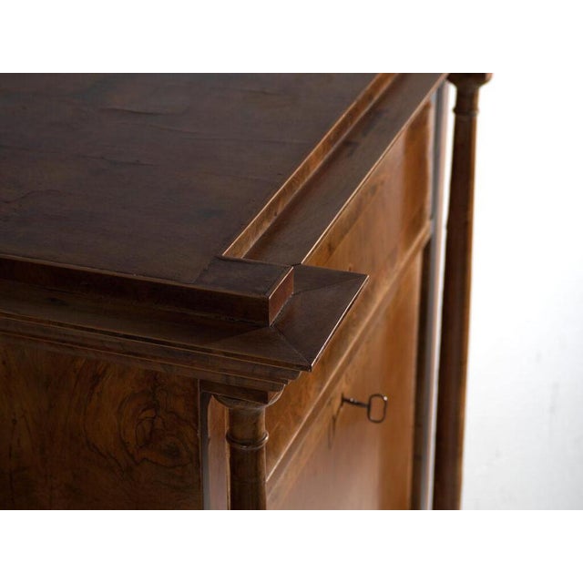 This antique biedermeier secrétaire in walnut wood features an architectural pediment over a symmetrical body with two...