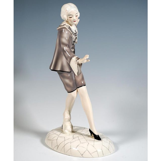 Delicate young dancer with ash-blonde, chin-length hair, wearing a grey costume comprising knee-length trousers and a...