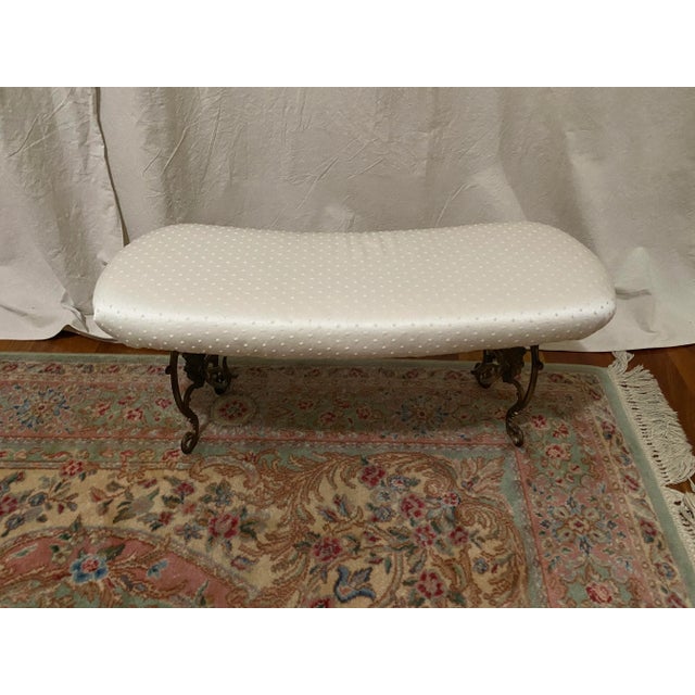 Slight kidney shaped romantic boudoir bench upholstered in a Swiss Dot Sateen fabric with ornate metal base.