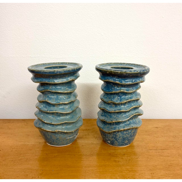 A pair of sculptural ceramic candle holders featuring stacked, undulating ridges and wide circular tops with recessed...