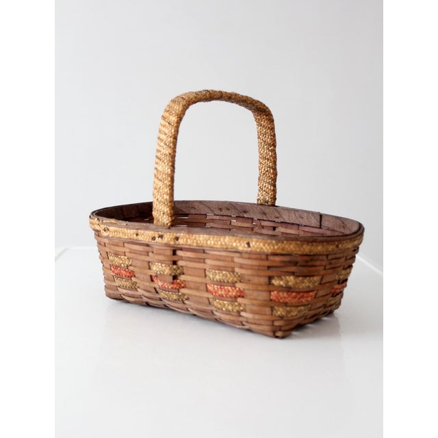 Vintage woven gathering basket featuring a wrapped handle, warm honey-brown finish, and woven accent bands that add subtle...