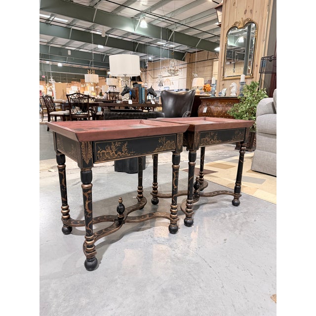 This is a striking pair of japanned chinoiserie tray tables featuring hand painted gold landscape scenes set against a...