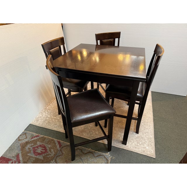 Design Plus Gallery presents a Bistro Dining Set in Dark Wood and Contemporary Styling. The four chairs have elevated bar...