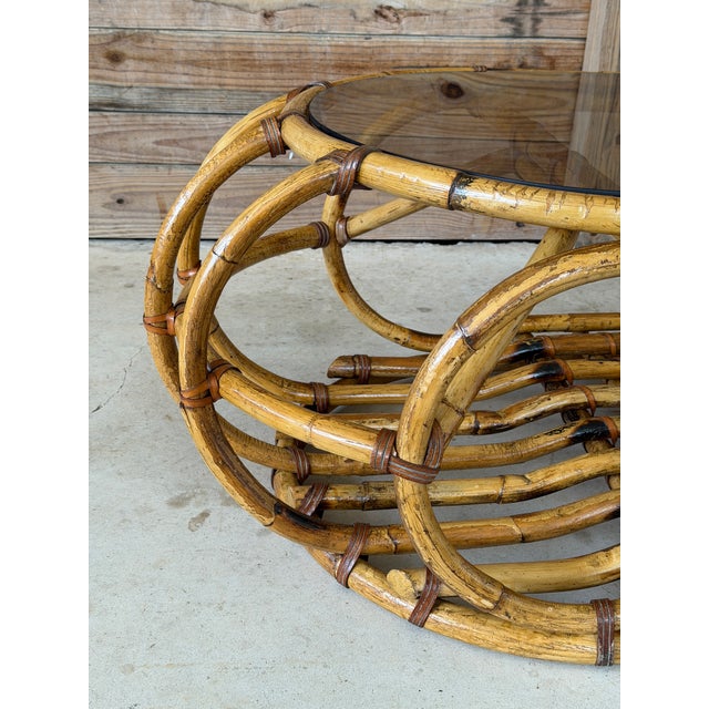 A gorgeous vintage coastal rattan coffee table featuring a sculptural wrapped frame and original smoked glass top. The...