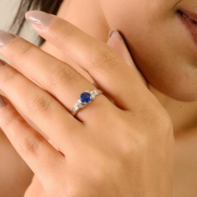 This elegant Art Deco-inspired ring features a 0.47-carat round-cut blue sapphire, approximately 4.8 mm in diameter, set...