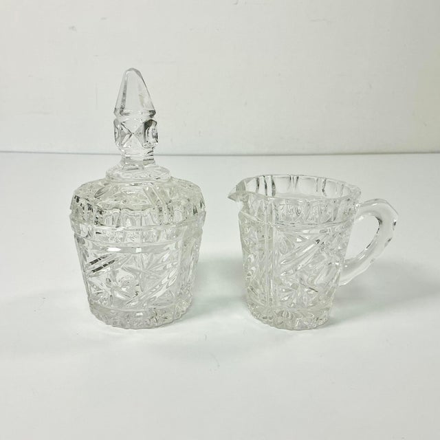 A lovely set of cut glass covered Sugar Bowl and Creamer. They feature a botanical cut design. The sugar lid has a large...
