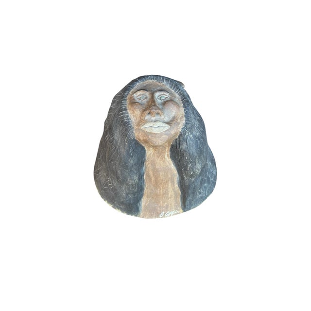 This sculpture of fired clay and pigment is a bust of a Native American woman with a feather in her hair gazing up at the...