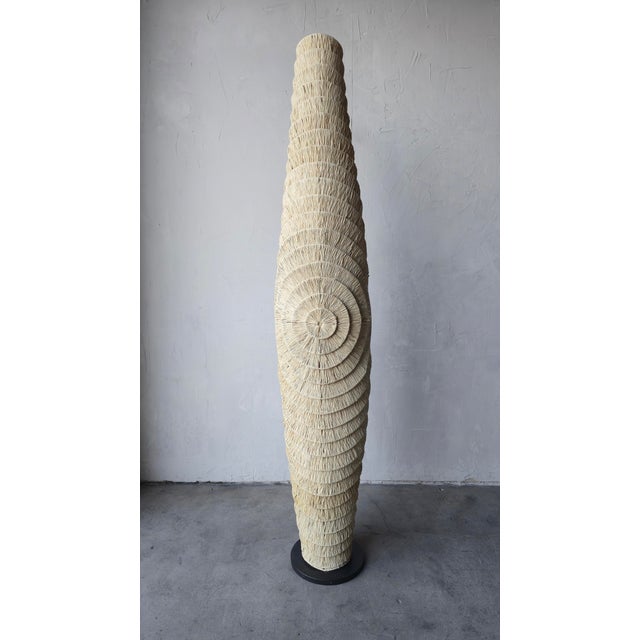 This is a striking sculptural floor lamp handcrafted from natural woven fiber over a metal frame. Its tall organic...