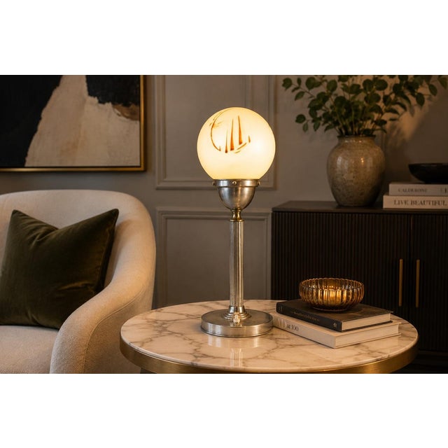 A striking vintage Art Deco / Machine Age table lamp featuring a frosted glass globe shade set above a streamlined metal...