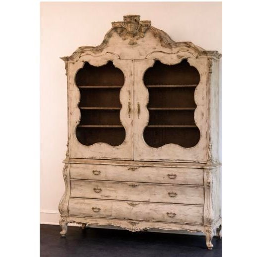 Distinctive serpentine (curved) doors Heavy hand-carved crest and apron at the top Painted, distressed white or cream...