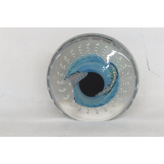 This wonderful Paper Weight is made of glass. This piece features a charming round shape, it is transparent with blue and...