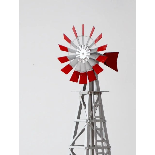 This is a vintage decorative windmill. The tall, gray wood windmill features red stripes across its sails. Slender wires...