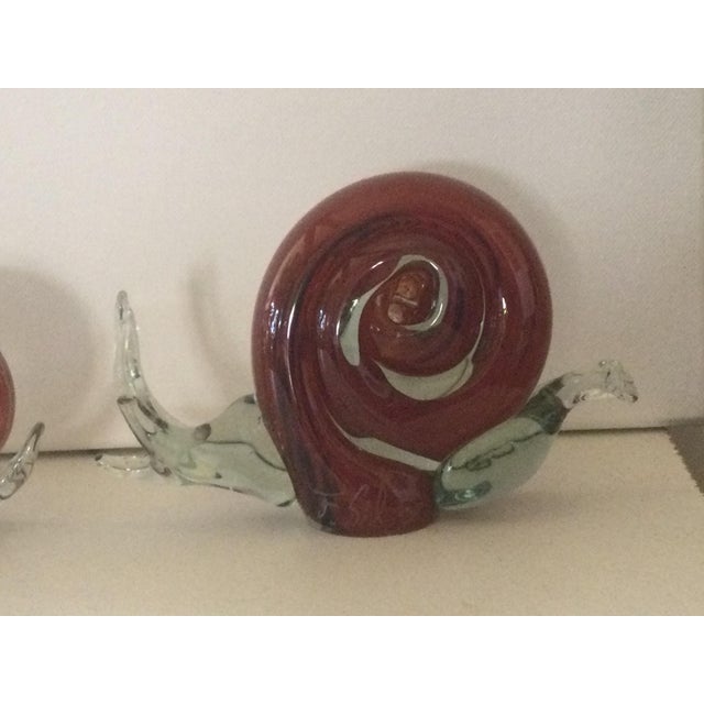 A family of three handmade art glass snails in decreasing sizes, signed by the artist Florea Silviu. The bodies are...