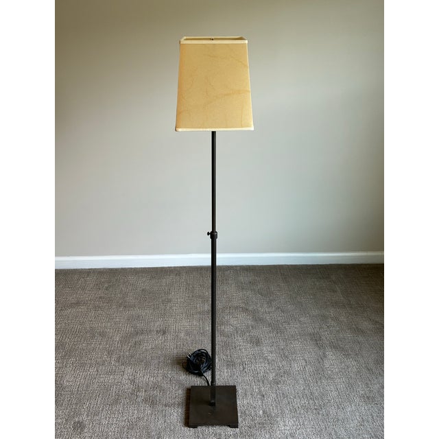 Elegant minimalist floor lamp featuring a slender adjustable stem rising from a clean square base in a rich dark bronze...