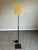 Elegant minimalist floor lamp featuring a slender adjustable stem rising from a clean square base in a rich dark bronze...