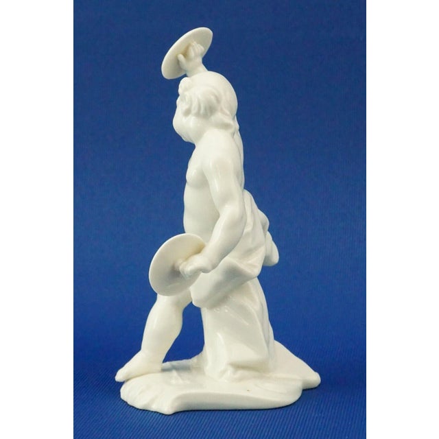 A sculpture in the finest white glazed porcelain depicting a cherub or putto with cymbals. Marked under the base with an...