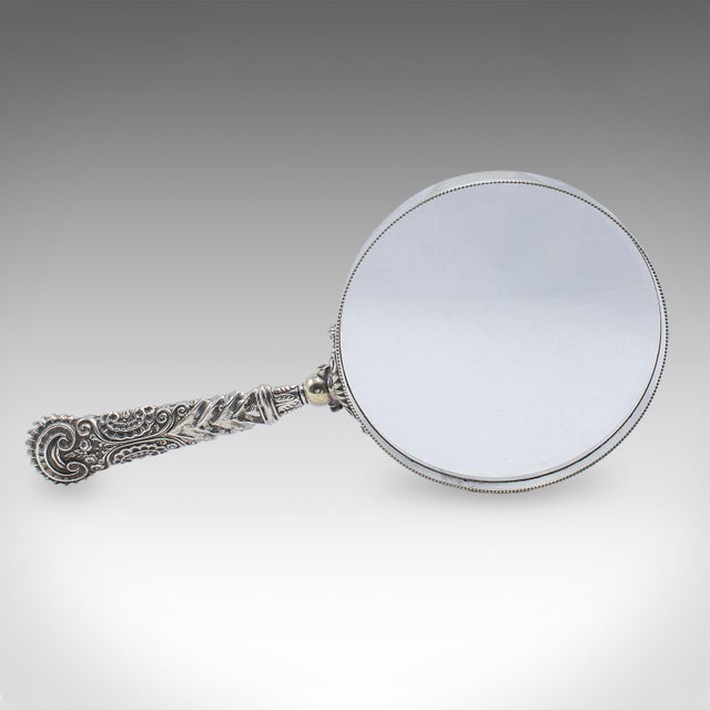 This is an antique reader's magnifying glass. An English, silver plated library magnifier, dating to the late Victorian...