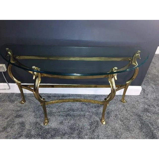 Substantial and beautifully stylized polished brass seahorse Demilune console with graceful curved and beveled glass top....