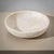 A large, heavy stone bowl crafted from beige travertine, featuring a minimalist design. The bowl is distinguished by its...