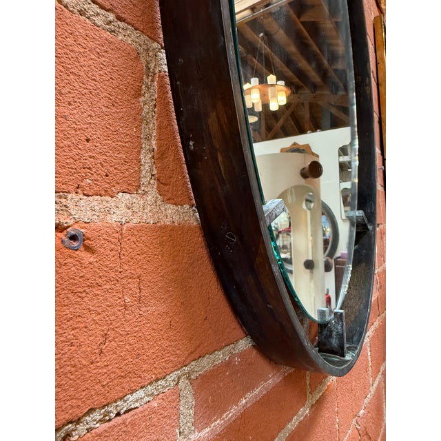 Striking vintage wall mirror featuring an elongated oval form set within a hand-forged iron frame. The dark patinated...