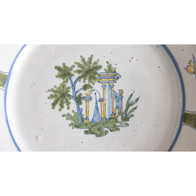 A classic 18th century Nevers green polychrome plate featuring a temple nested amongst trees; the scalloped rim adorned...