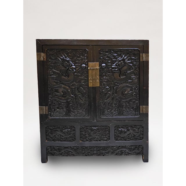 Each rectangular cabinet stained a deep purply brown and fitted with two doors deeply carved with dragons in pursuit of a...