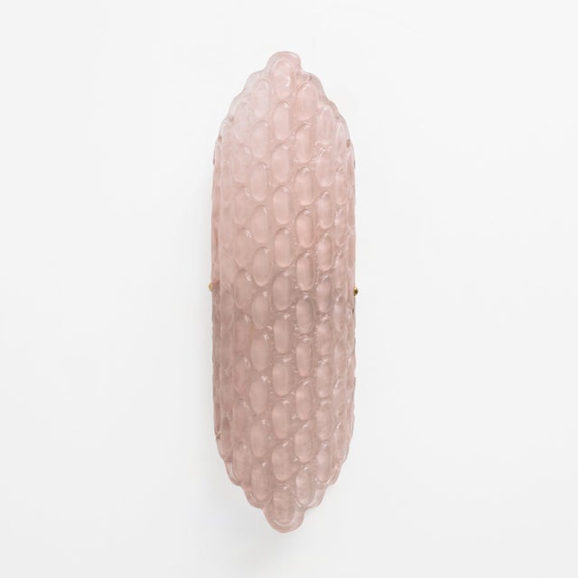 Elegant pair of wall sconces featuring large diffusers in soft blush-pink Murano glass, handcrafted with a refined relief...
