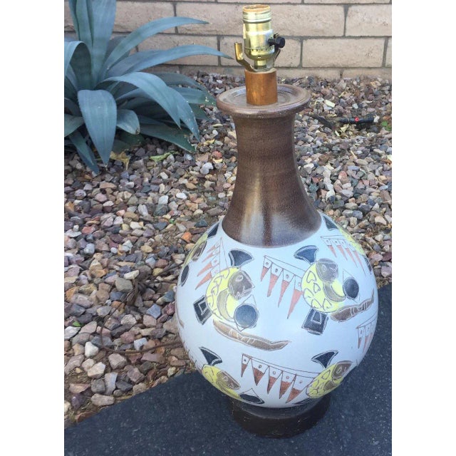 Mid century modern pottery table lamp. Features abstract incised fish and flag design with metal base and wood collar....